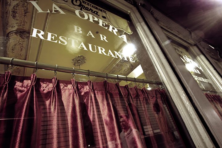 Puerta de vidrio con las letras doradas Bar Restaurante La Opera y cortina de terciopelo guinda detrás